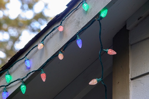 How To Hang Christmas Lights Safely (Tips From A Professional Roofer in Covington, LA ) Pride Roofing LLC. closeup image of multi colored christmas lights being hung on pitch of roof on house
