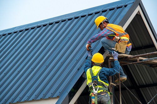 What Things Affect Your Commercial Roofing Service Lifespan? | Pride Roofing LLC in Albany, LA. Image of roofers using air or pneumatic nail gun and installing metal roof tile on top of a new building.