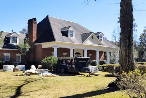 Winter-proof your home in New Orleans with essential roofing tips with Pride Roofing LLC in Hammond, LA. Image of a beautiful house with roofing shingles in the yard, ready for installation to winter-proof the home.