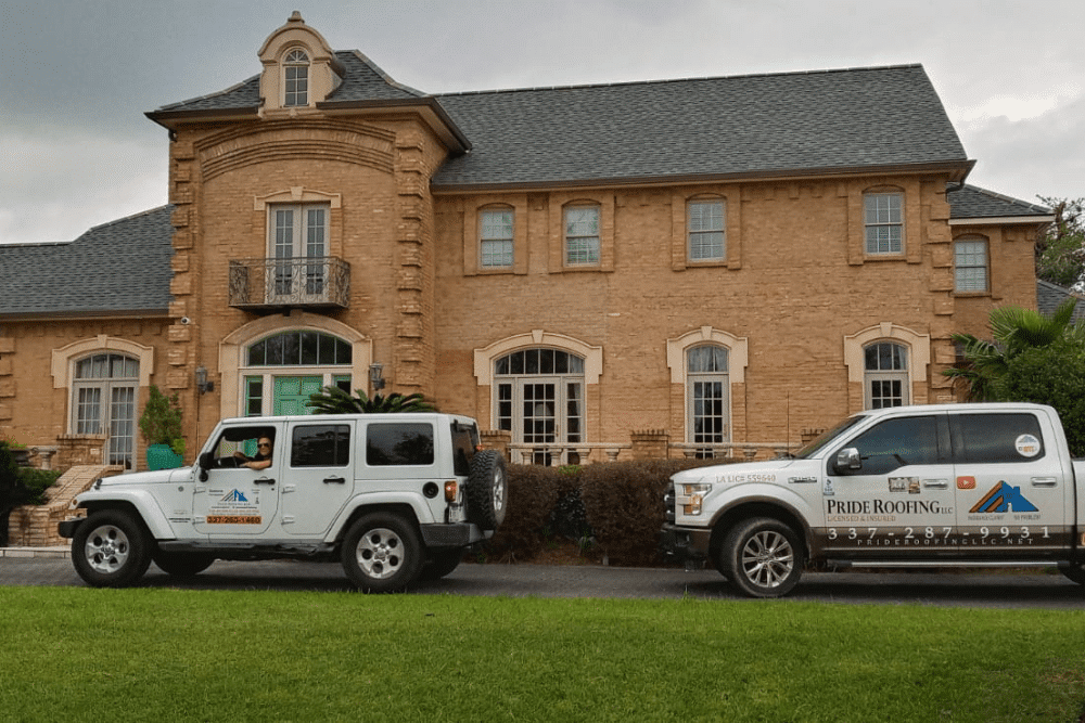 Emergency roof leak repair, roof services in Hammond, LA by Pride Roofing LLC. Image of branded service vehicles parked in front of a large brick home, showcasing trusted residential roofing solutions.