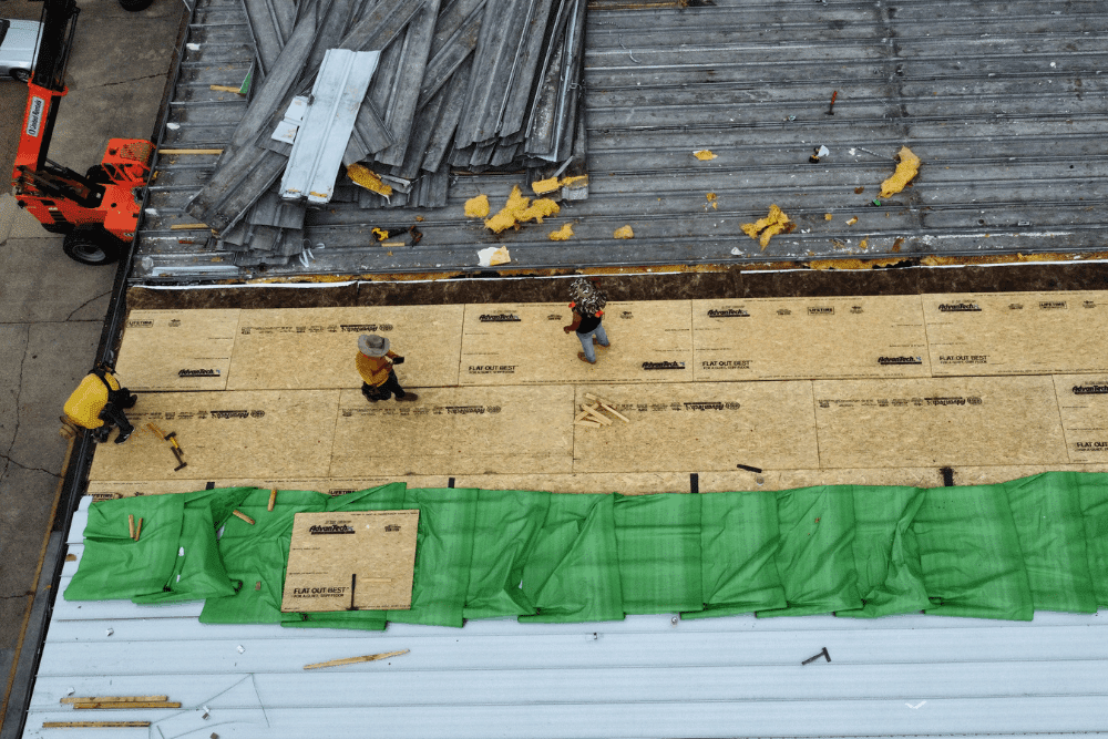 Roof replacement, roofing services in Hammond, LA by Pride Roofing LLC. Image of roofing professionals installing decking and preparing a commercial roof surface, showing tear-off and rebuilding stages of a flat metal roof replacement.
