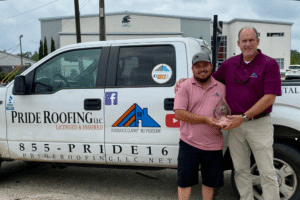 Roof replacement contractor in Baton Rouge, LA at Pride Roofing LLC. Image of two team members holding an award beside a branded Pride Roofing LLC work truck outside the company building.