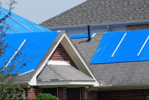 Fall roof maintenance, roofing services in Hammond, LA at Pride Roofing LLC. Image of a shingle roof partially covered with blue protective tarps during roof repair or maintenance.